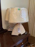 Pair of ceramic lamps with fan-shaped bases and pleated fabric shades, placed on wooden furniture.