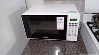 White Sunbeam microwave oven model SGCMV207WE07 on granite countertop next to stove, showing front door with black tinted window and digital control panel with keypad and display set to 15:40.