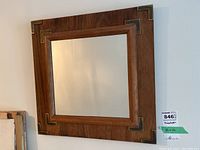 Frontal image showing entire square mirror with wood frame and metal corner trims.