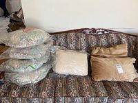 Couch with pillows displayed: four round 16-inch pastel pattern pillows vacuum sealed, and three rectangular pillows including cream ribbed and tan velvety fabrics.