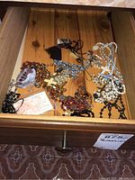 Drawer open showing assorted rosaries and religious cards spread out inside drawer on wooden surface.