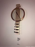 Full view of Seiko wall clock showing circular bronze frame, clock face with gold central panel, black hands, and rectangular metallic pendulum pieces below.