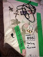 Photo showing multiple jewelry items including sterling silver chains with pendants, packaged earrings, rings, and a Murano glass pendant label with lot number.