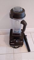 Vitamix blender assembled with container, lid, and tamper on a tiled floor.