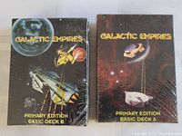 Photo showing two sealed Galactic Empires card decks titled Primary Edition Basic Deck A and Basic Deck B with space-themed artwork.
