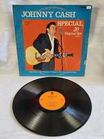 Photo of the vinyl record with the orange label and visible grooves, and the front of the album cover showing Johnny Cash with a guitar against an orange and blue background.