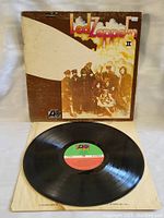 Photo showing the vintage Led Zeppelin II album cover with visible edge wear and the black vinyl record laid in front, showing the original Atlantic Records label.