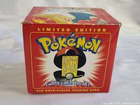 Box of limited edition Pokémon ball with 23k gold-plated trading card, shows front of box with branding and card image.