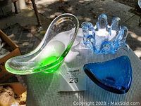 Top view of three art glass bowls, elongated green & clear bowl on left, blue wavy-edged bowl top right, triangular blue mini bowl bottom right.