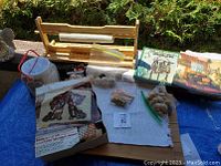 Overview of lot showing wooden craft paper cutter, bead holder container with beads, latch hook kit box, books, and fabric canvas.