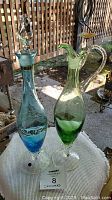 Photo showing blue glass decanter with gold detailing and green glass pitcher on stand outdoors