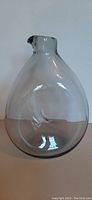 Clear smokey glass decanter with bird beak shaped spout, shown front view on plain background.
