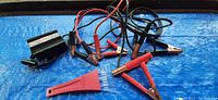 Two sets of jumper cables with red and black clamps and insulated handles visible alongside a mobile power inverter on blue tarp.