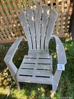 Front view of the gray plastic Adirondack patio chair showing slatted backrest and seat, and wide armrests.