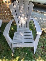 Front view of brown lightweight plastic Adirondack chair with slatted seat and back and wide armrests.