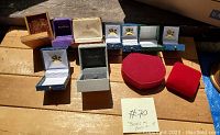 Full assortment of 12 assorted ring boxes arranged on a wooden surface, showing variety of colors and materials
