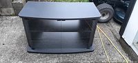 Front view of black laminated TV stand with two glass doors and single internal shelf, placed outdoors on concrete