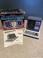 Full view of Tandy Alien Chase electronic game on tabletop with original outer box and instruction manual accompanying it.