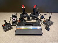 Full lot including Atari 2600 console, joysticks, flight stick controllers, power adapter, and cables arranged on tabletop.