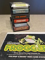Stack of six Atari game cartridges. Visible labels read Frogger, Seaquest, Star Raiders, Freeway, Frogs and Flies, River Raid.