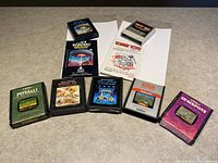 All 7 Atari game cartridges with 2 instruction manuals spread on flat surface, showing titles and artwork.