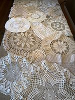 Overview photo showing multiple handmade crochet doilies arranged on a flat surface, displaying various sizes and intricate patterns in cream colors.