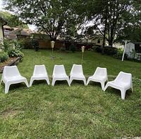 Front view of six white IKEA Bunsö chairs arranged outdoors on grass. Five chairs are available as described in seller note, showing stackable molded plastic design.