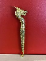 Full view of the golden dragon letter opener showing the full body and tail on red background.