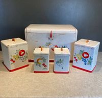 Front view of the vintage metal bread box and four matching painted fruit canisters arranged in a row.