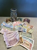A mason jar filled with coins alongside a spread of various international paper bills including Korean and Japanese currency.
