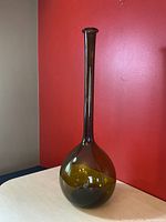 Front view of an olive green tall glass decanter with a long slender neck and bulbous base, set against red background.