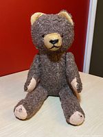 Front-facing view of the vintage Steiff teddy bear with grey mohair, yellow felt snout and ears, and beige paw pads showing wear.