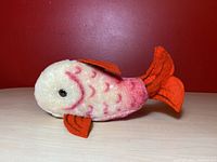 Full side view of the red and white Steiff Flossy fish plush on a light surface with red background.