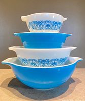 Four bowls stacked alternating patterned white and solid turquoise, showing handles and spouts