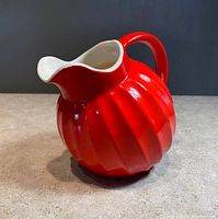 Angle view of the bright red ribbed ceramic pitcher with a smooth white interior and a flared spout.