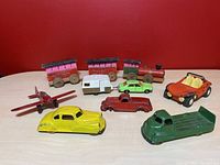 Overview of the lot showing multiple vintage toys including wooden train with pink and brown cars, red airplane, and various toy cars and trucks in multiple colors.