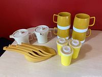 Front view of all 14 kitchenware items arranged on table against red background, showing thermos mugs, Tupperware shakers, Foley scoops, and harvest gold ladles.