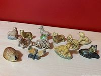 Overview of 12 small animal figurines including hedgehog, butterfly, horse, and various dog breeds on a wooden surface