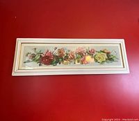 Full view of the white framed panoramic floral roses print hanging on a red wall, showing overall condition and frame.