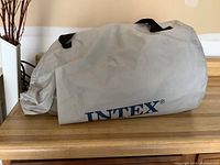 Grey carrying bag with black straps and Intex branding, containing the deflated air bed