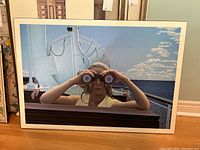 Framed poster showing a woman with binoculars on a ship deck with ocean background.