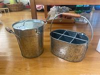 Photo of galvanized metal 6 bottle carrier with wooden handle beside a galvanized metal ice bucket with lid and side handles, both items shown on a wooden floor.