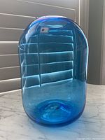 Side view of the blue glass vase, showing smooth elongated cylindrical form with light reflections and clarity of glass.