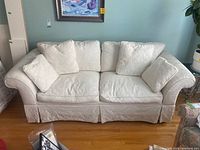 Front view of cream fabric sofa with cushions, showing floral pattern and rolled arms.