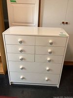 Front view of the white IKEA dresser showing 8 drawers with round knobs, some scratches visible on surface.