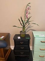 Full view of nightstand with faux orchid plant on top, showing front and decorative elements.