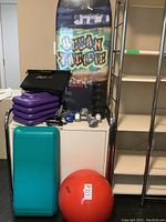 Wide view of aerobic step platforms, dumbbells, exercise ball, black back roller, and Ocean Pacific boogie board standing behind.
