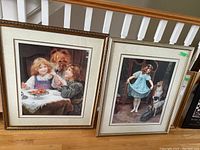 Photo showing both framed prints leaning against a white staircase banister on wooden floor