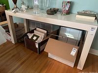 Full view of white Parsons style table with various decorative items on top and boxes underneath.