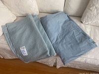 Photo showing folded light blue duvet cover and matching pillow shams on white floral couch.
